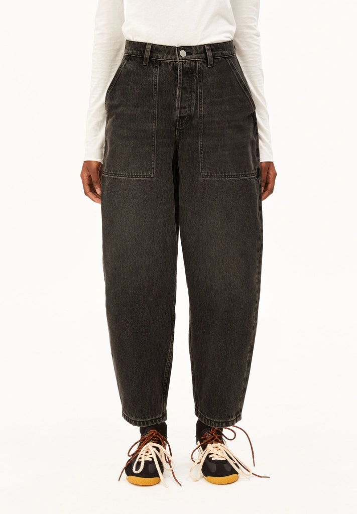 Woman wearing ARMEDANGELS Canada Baarly Barrel Jeans in Nutmeg washed black with a white long-sleeve top and sneakers, front view against a white background.