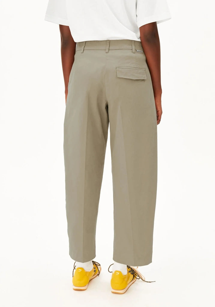 A person shown from the back wearing light khaki cropped trousers, a white short-sleeve top, and bright yellow sneakers against a plain white studio background.