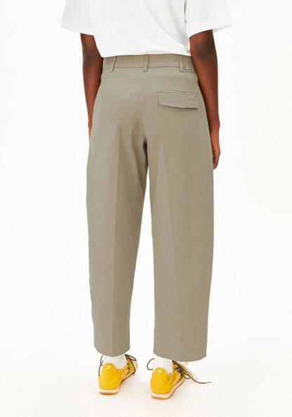 A person shown from the back wearing light khaki cropped trousers, a white short-sleeve top, and bright yellow sneakers against a plain white studio background.