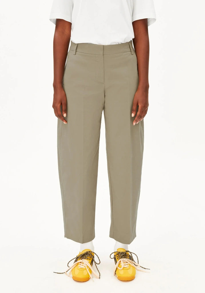 A model wearing a pair of high-waisted, wide-leg cropped trousers in a muted sage green color, styled with a white t-shirt and yellow sneakers against a plain white background.