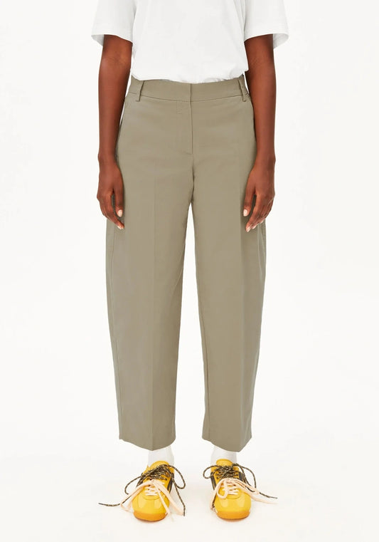 A model wearing a pair of high-waisted, wide-leg cropped trousers in a muted sage green color, styled with a white t-shirt and yellow sneakers against a plain white background.