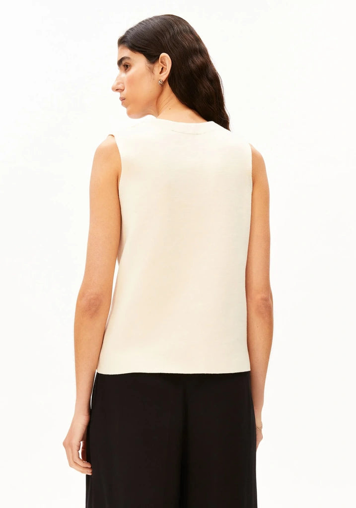 Back view of a woman wearing the ARMEDANGELS Canada Compact Buttoned Knit Vest in oatmilk with black trousers against a white background.
