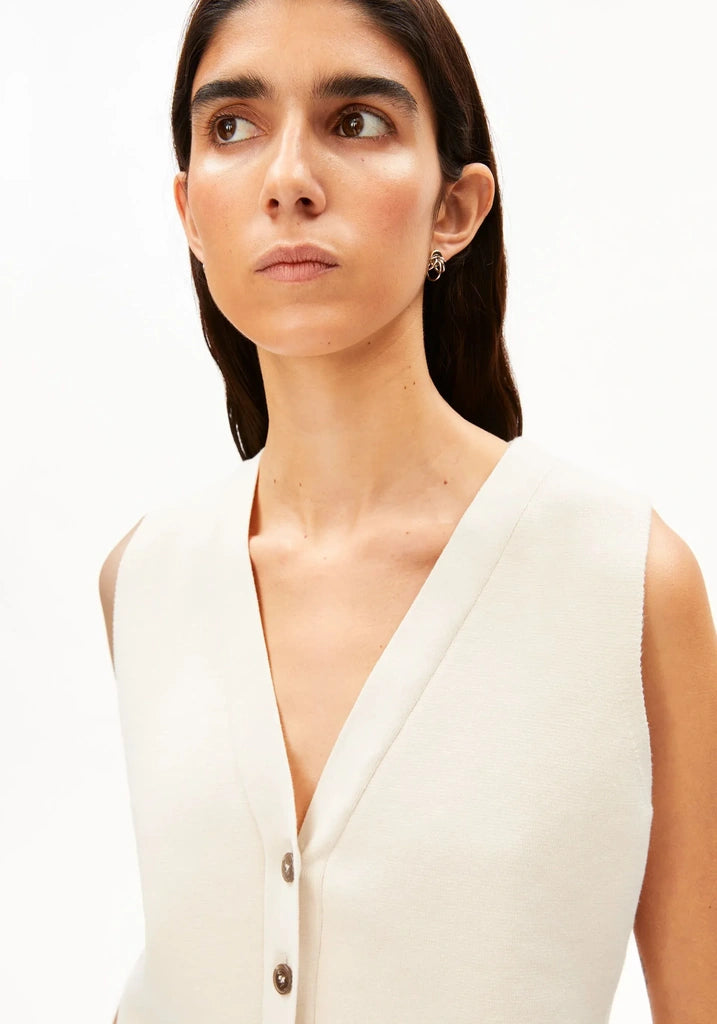 Close-up of the deep V-neck and tortoise-look buttons on the ARMEDANGELS Canada Compact Buttoned Knit Vest in oatmilk, worn by a woman against a white background.
