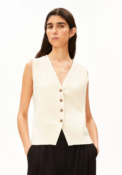 Woman wearing the ARMEDANGELS Canada Compact Buttoned Knit Vest in oatmilk with black pleated trousers, front view against a white background.
