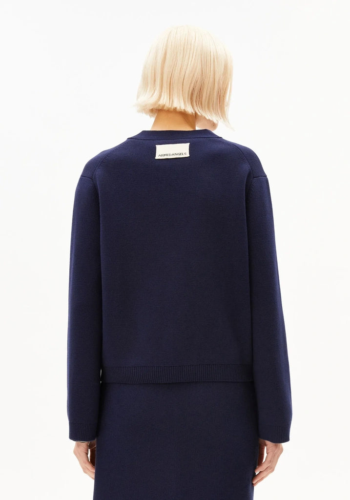 A model viewed from the back wearing a navy blue knit sweater and matching skirt against a plain white studio background.