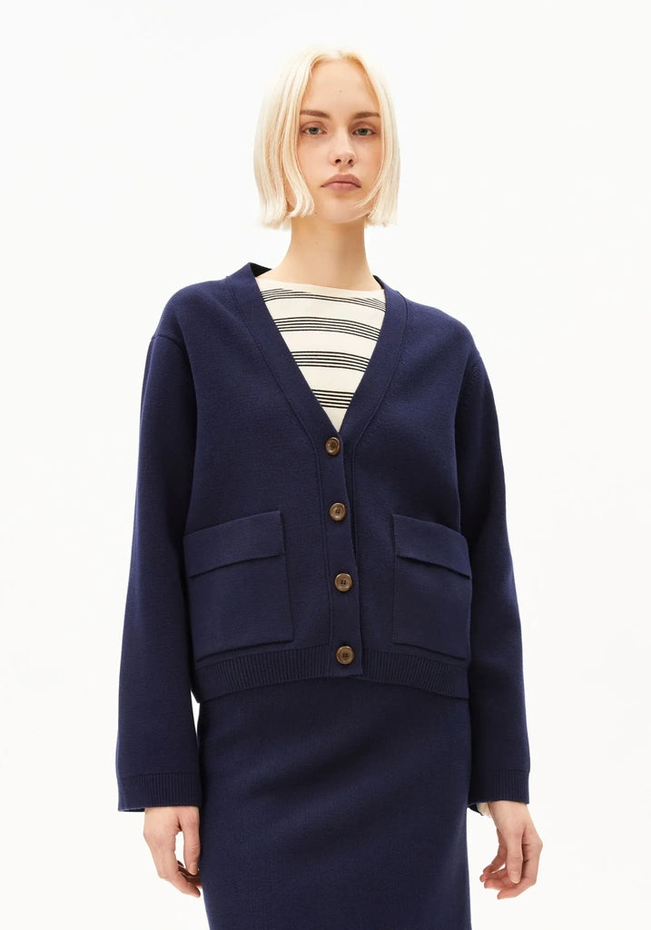 A model with short blonde hair wearing a navy blue cardigan over a black and white striped top, paired with a matching navy skirt, against a plain white background.