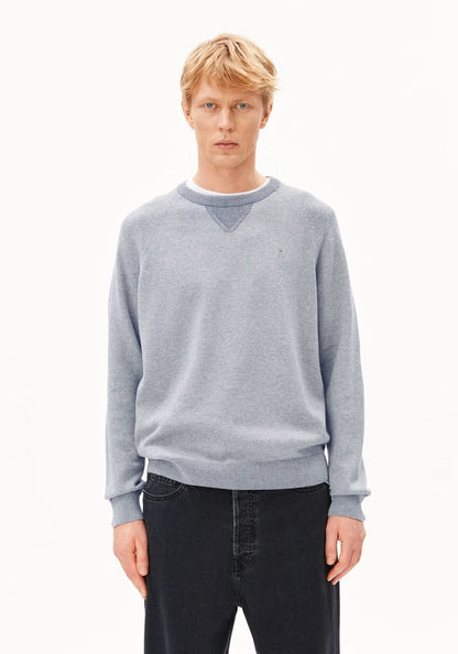 A blonde male model wearing a light gray heathered crewneck sweater with a small embroidered polo player logo on the left chest, paired with dark jeans, against a plain white studio background.