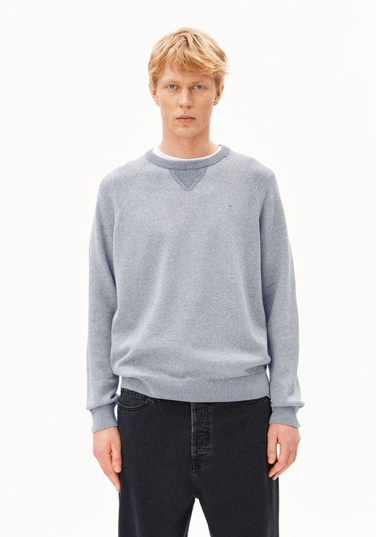 A blonde male model wearing a light gray heathered crewneck sweater with a small embroidered polo player logo on the left chest, paired with dark jeans, against a plain white studio background.