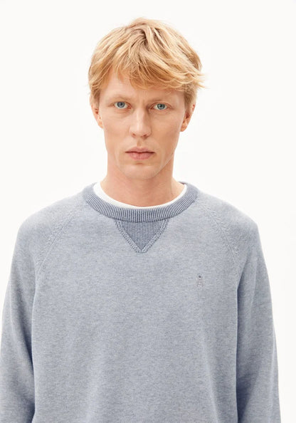 A blonde male model wearing a light gray heather crewneck sweater with a subtle embroidered polo player logo on the left chest, set against a plain white background.