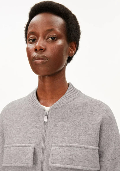 A close-up shot of a model wearing a light gray zip-up bomber jacket with two front patch pockets, set against a plain white studio background.