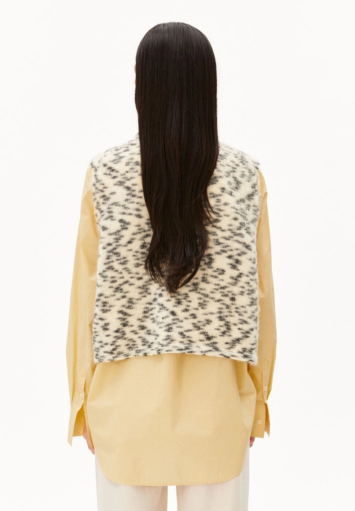 Back view of a woman wearing ARMEDANGELS Canada Dotted Mohair-Blend Knit Vest in Oatmilk-Black over a yellow shirt, against a white background.