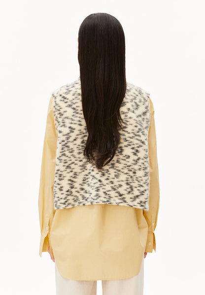 Back view of a woman wearing ARMEDANGELS Canada Dotted Mohair-Blend Knit Vest in Oatmilk-Black over a yellow shirt, against a white background.