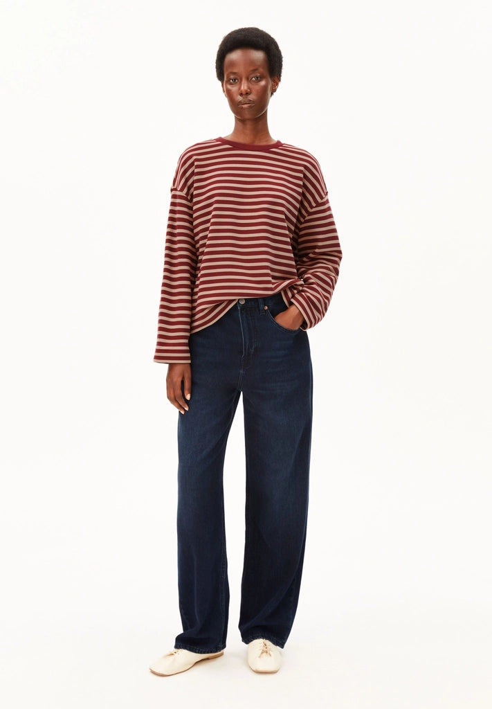 Full-length front view of a woman wearing ARMEDANGELS Canada Frankaa Maarlen Stripe Sweatshirt in Velvet Red-Honey Reed with dark wide-leg jeans and white flats, against a white background.