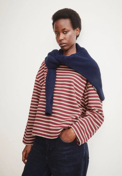 Woman wearing ARMEDANGELS Canada Frankaa Maarlen Stripe Sweatshirt in Velvet Red-Honey Reed with a navy sweater draped over her shoulders, against a light grey background.