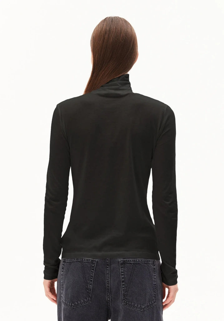 A woman viewed from the back wearing a black long-sleeve mock neck top and dark gray jeans against a plain white background.