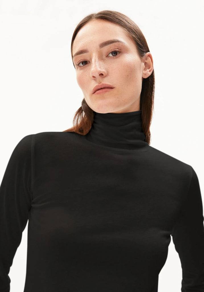 Woman wearing a black turtleneck longsleeve shirt against a white background