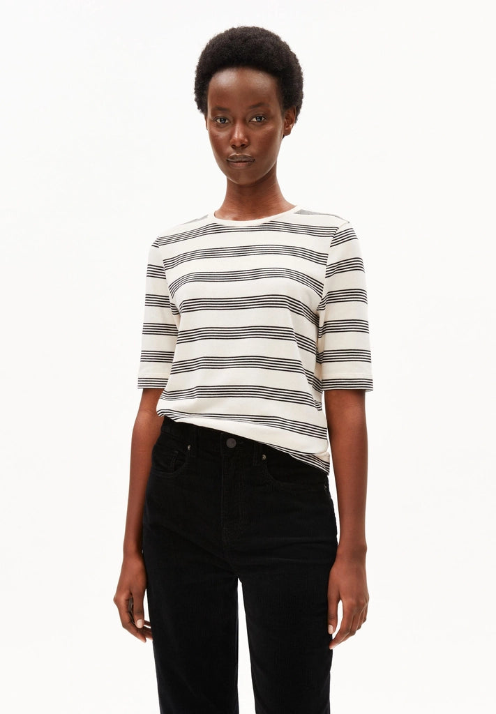 Woman wearing ARMEDANGELS Canada Jaanisara Fine Stripe T-Shirt in Oatmilk-Black with black jeans, front view against a white background.