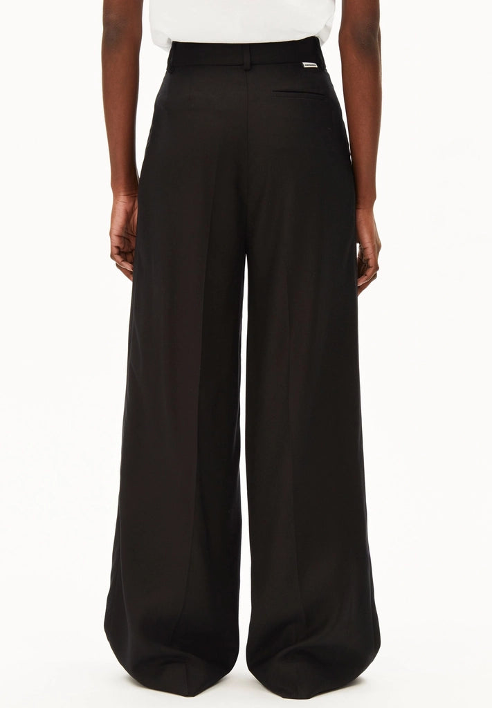 Back view of a woman wearing ARMEDANGELS Canada Kaayua Wide Leg Pants in black with a white tee on a white background.