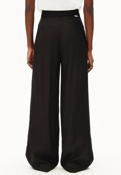 Back view of a woman wearing ARMEDANGELS Canada Kaayua Wide Leg Pants in black with a white tee on a white background.
