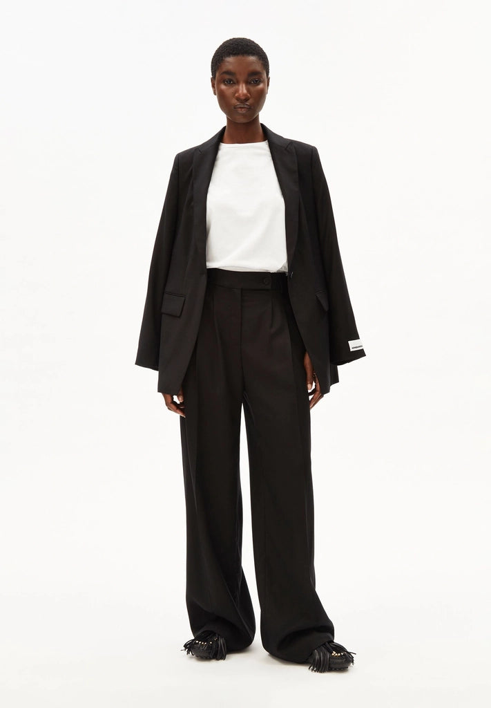 Full-length front view of a woman wearing ARMEDANGELS Canada Kaayua Wide Leg Pants in black with a white tee and a black blazer over her shoulders, on a white background.