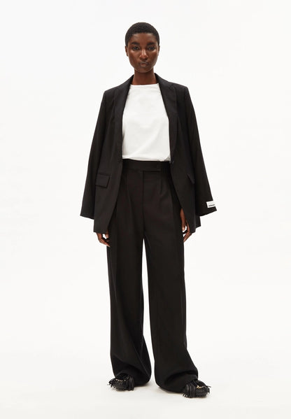 Full-length front view of a woman wearing ARMEDANGELS Canada Kaayua Wide Leg Pants in black with a white tee and a black blazer over her shoulders, on a white background.