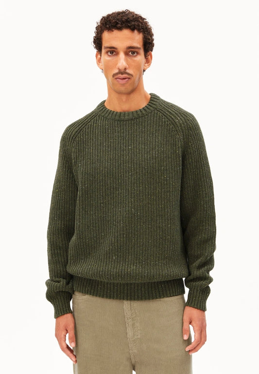 Man wearing the ARMEDANGELS Canada Kiaano Tweed Knit Sweater in dark olive green with beige corduroy trousers on a white studio background.