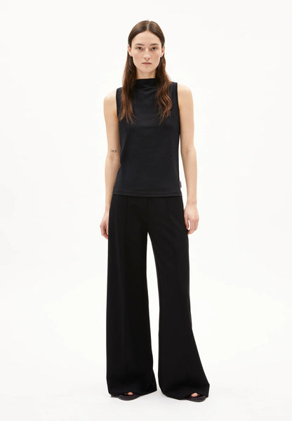 Full-length front view of a woman wearing the ARMEDANGELS Canada Laminiaa Sleeveless Top in black with black wide-leg trousers on a white background.