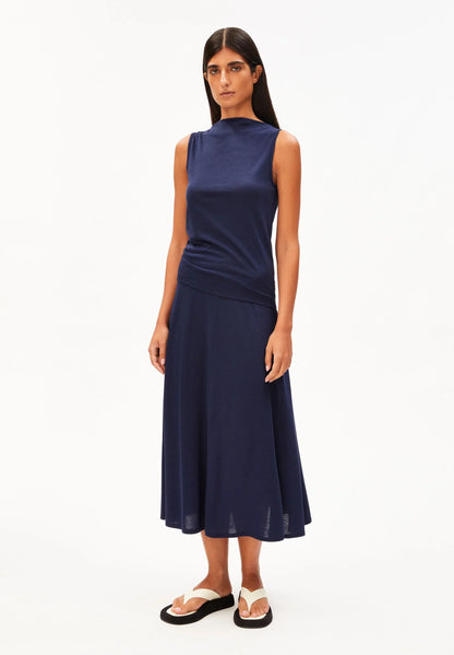 Full-length front view of a woman wearing the ARMEDANGELS Canada Laminiaa Sleeveless Top in tinted navy with a navy midi skirt and white sandals on a white background.