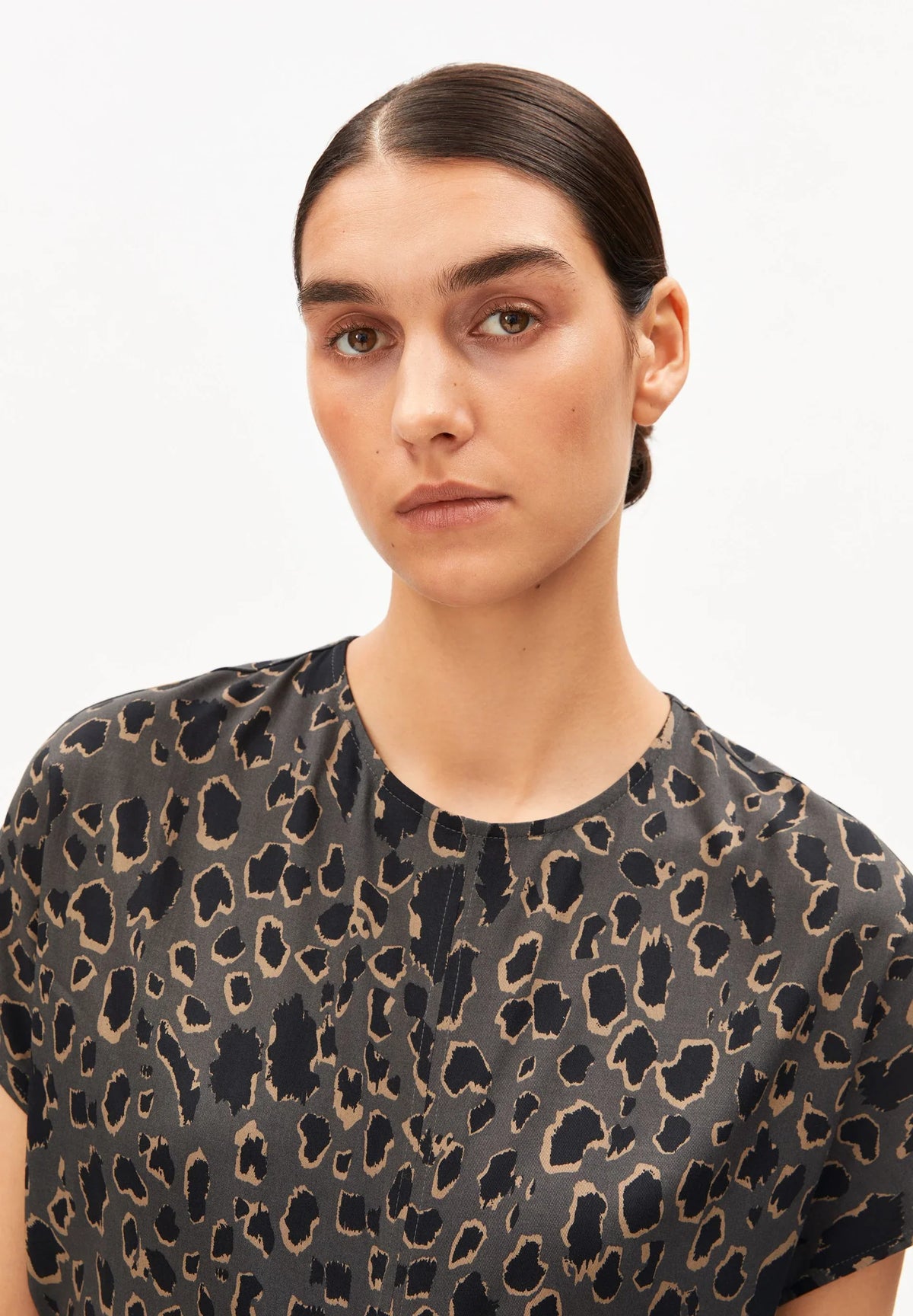 Close-up of the round neckline and leopard print on the ARMEDANGELS Canada Leo Bat Wing Midi Dress, worn by a woman against a white background.