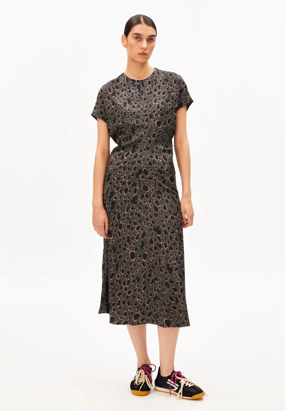 Full-length front view of a woman wearing the ARMEDANGELS Canada Leo Bat Wing Midi Dress in leopard print with black sneakers on a white background.