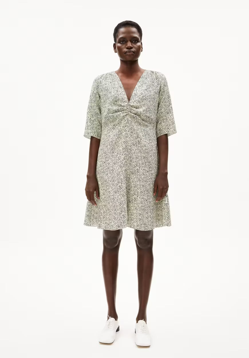 Full-length view of a woman in the ARMEDANGELS Canada Lilaat Waterdrop Dress in seagreen, a knee-length printed dress worn with white sneakers, against a white background.