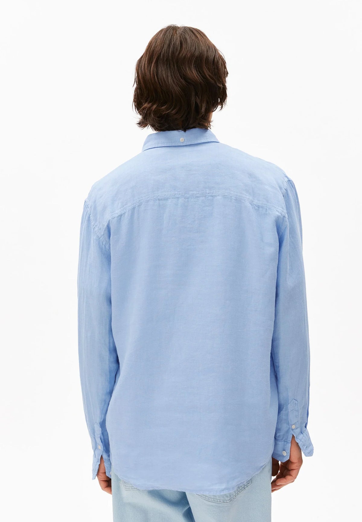Back view of a man wearing the ARMEDANGELS Canada Linen Longsleeve Shirt in Wedgwood blue with light jeans on a white background.