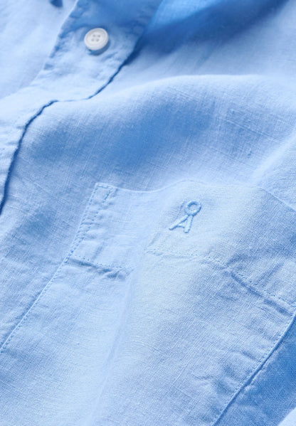 Close-up of the linen texture and tonal logo embroidery on the chest pocket of the ARMEDANGELS Canada Linen Longsleeve Shirt in Wedgwood blue.