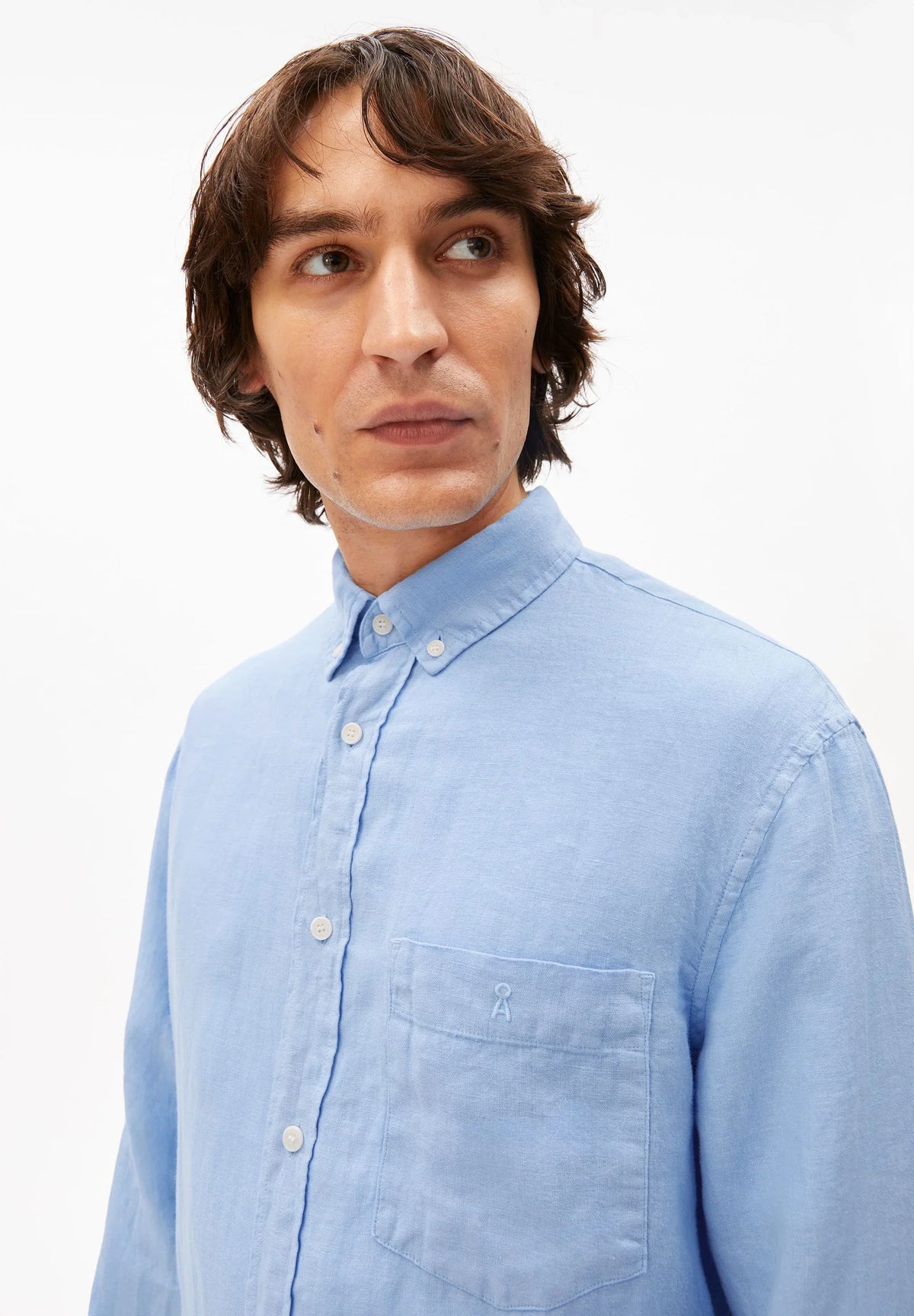 Close-up of the collar, buttons and chest pocket on the ARMEDANGELS Canada Linen Longsleeve Shirt in Wedgwood blue, worn by a man.