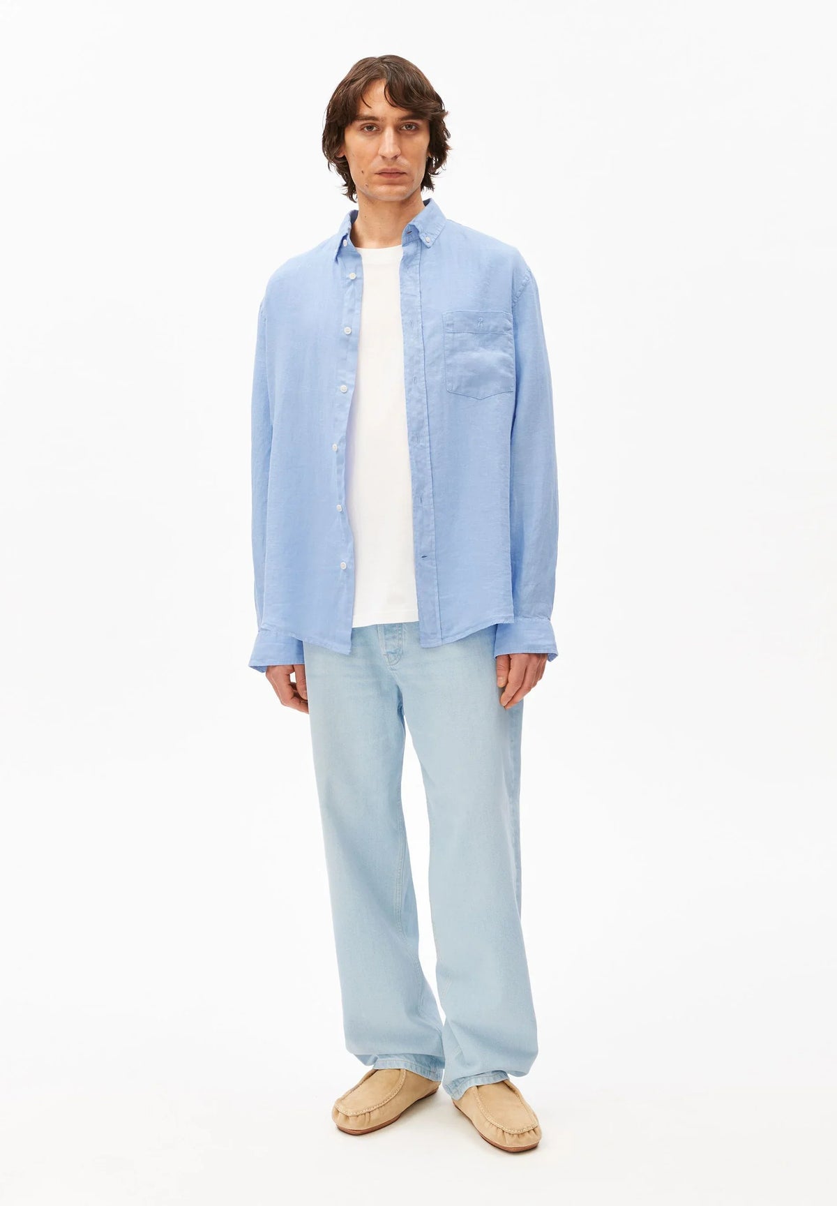Full-length front view of a man wearing the ARMEDANGELS Canada Linen Longsleeve Shirt in Wedgwood blue with a white tee, light-wash jeans and suede shoes on a white background.