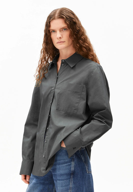 Woman wearing a dark gray button-up shirt and blue jeans on a white background