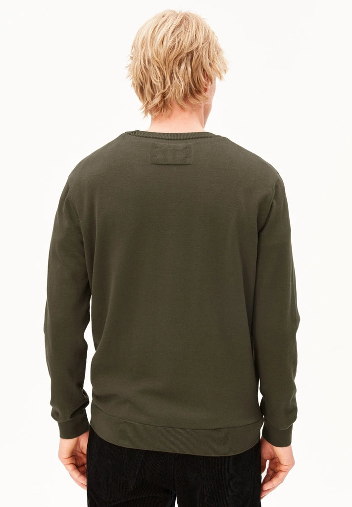 Back view of a man wearing the ARMEDANGELS Canada Loukaa Knit Sweater in dark earth with black trousers on a white background.