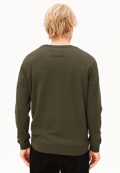 Back view of a man wearing the ARMEDANGELS Canada Loukaa Knit Sweater in dark earth with black trousers on a white background.