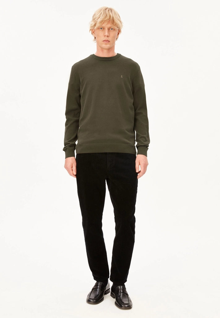 Full-length front view of a man wearing the ARMEDANGELS Canada Loukaa Knit Sweater in dark earth with black trousers and black leather shoes on a white background.