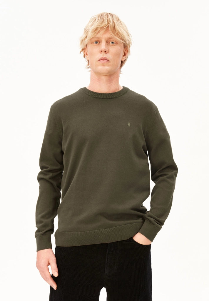 Man wearing the ARMEDANGELS Canada Loukaa Knit Sweater in dark earth olive with black trousers, front view on a white background.