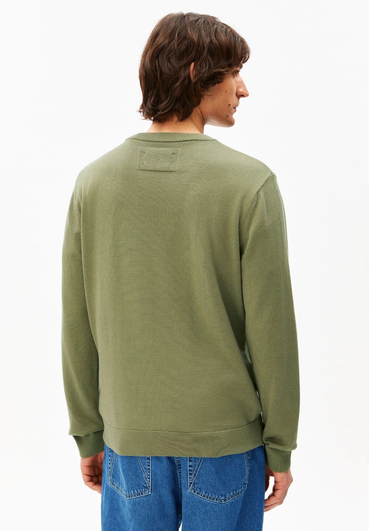 Back view of a man wearing the ARMEDANGELS Canada Loukaa Knit Sweater in fatigue green with jeans on a white background.