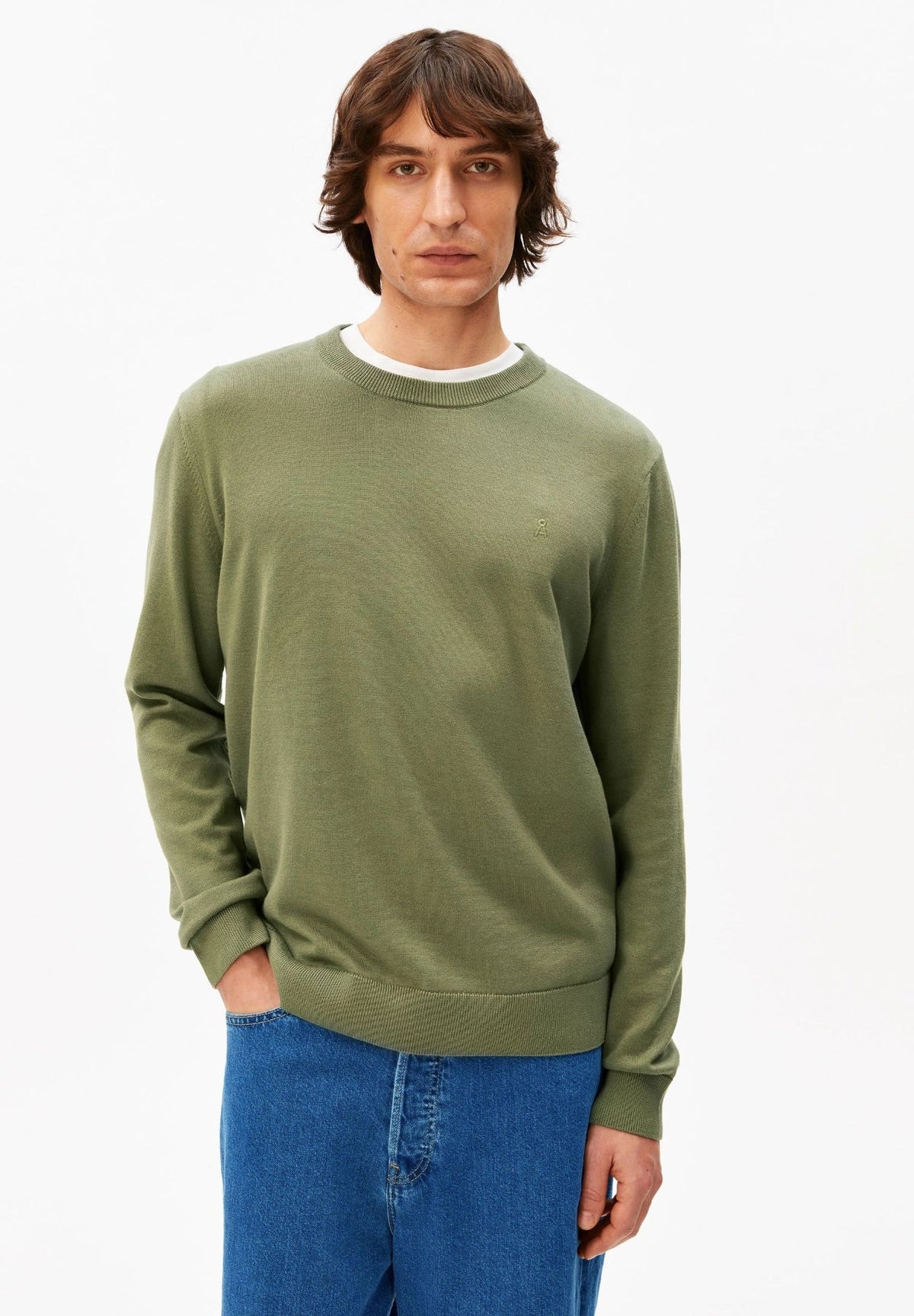 Man wearing the ARMEDANGELS Canada Loukaa Knit Sweater in fatigue green over a white tee with blue jeans, front view on a white background.