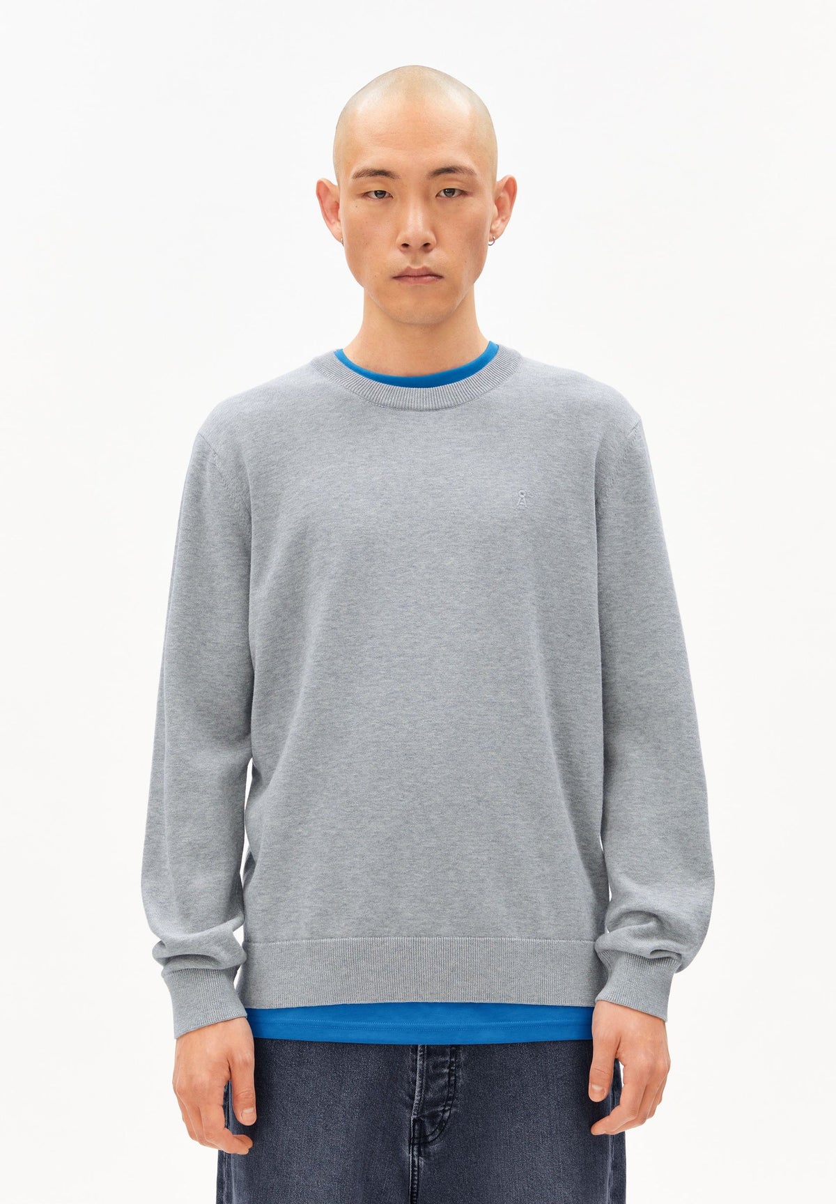 Man wearing the ARMEDANGELS Canada Loukaa Knit Sweater in silver melange grey over a blue tee with dark jeans, front view on a white background.