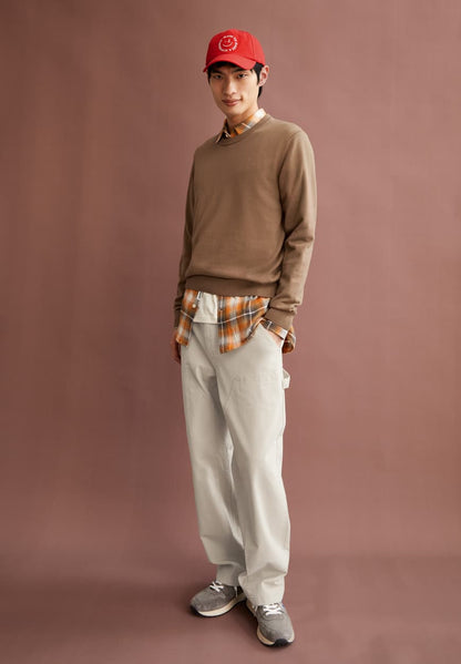 Men's casual outfit by ARMEDANGELS with brown sweater, plaid shirt, beige pants, red cap, and gray sneakers