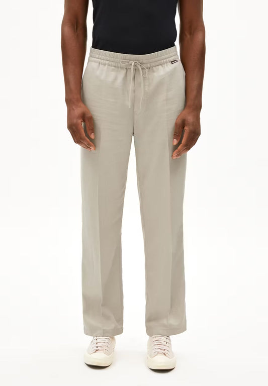Front view of a man wearing the ARMEDANGELS Canada Lukaa Lino Pant in sandstone with a black tank top and white sneakers, showing the drawstring waistband, on a white background.