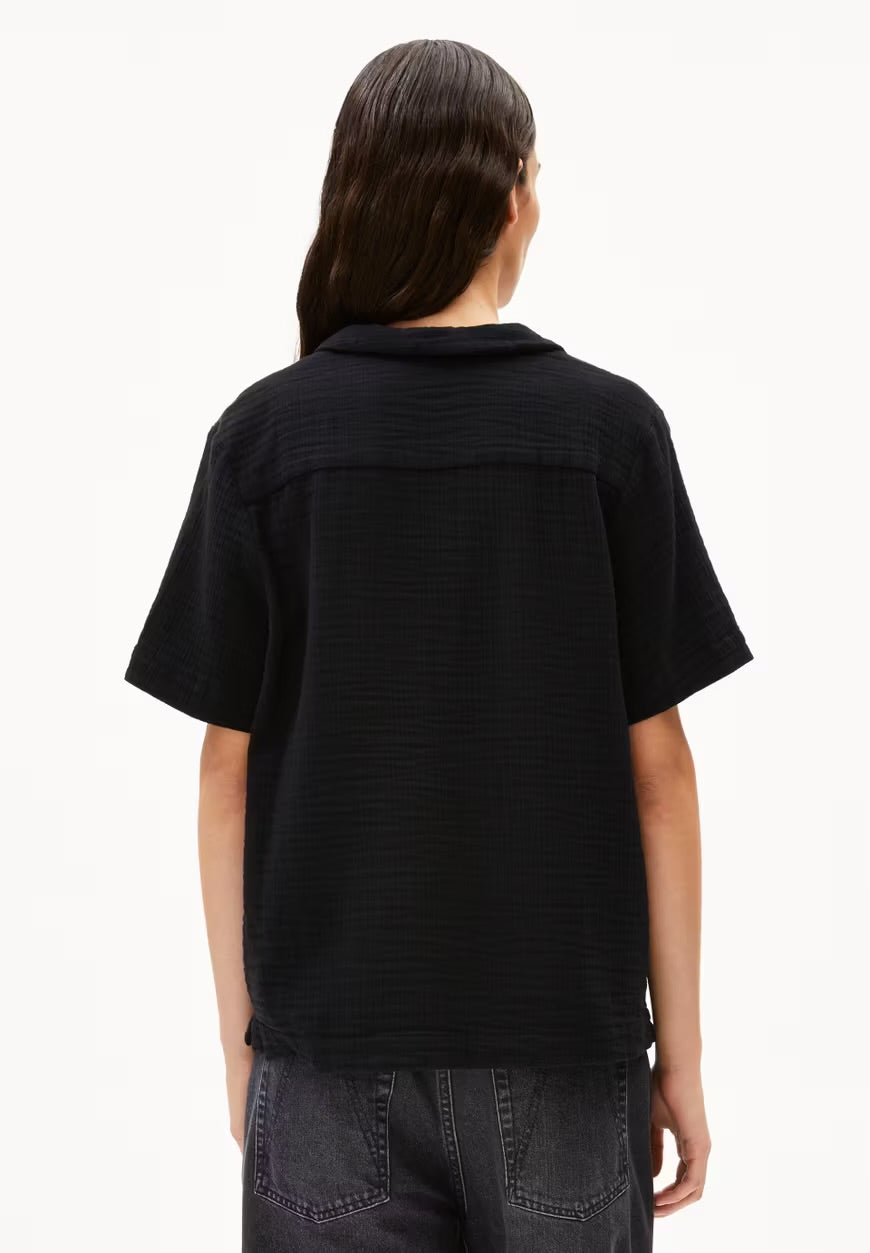 Back view of the ARMEDANGELS Canada Maaite Musselin Blouse in black, showing the back yoke and relaxed short sleeves, worn with grey jeans against a white background