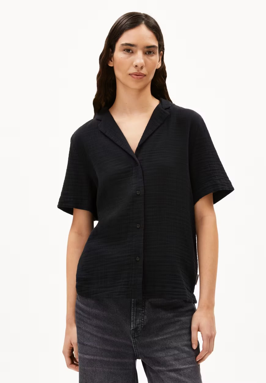Front view of a woman in the ARMEDANGELS Canada Maaite Musselin Blouse in black, buttoned up and worn with grey jeans, against a white background.