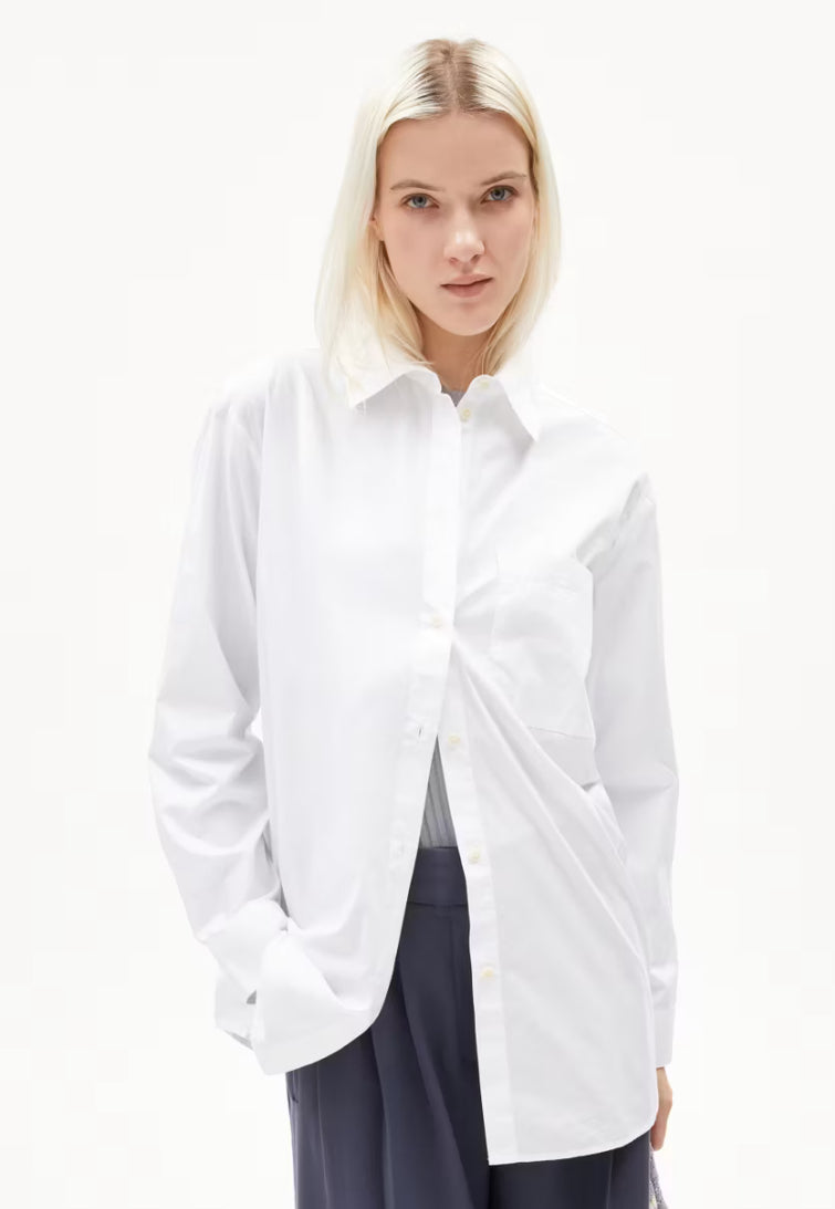 Woman wearing the ARMEDANGELS Canada Maalgaa Blouse in white, open over navy trousers, front view on a white background.