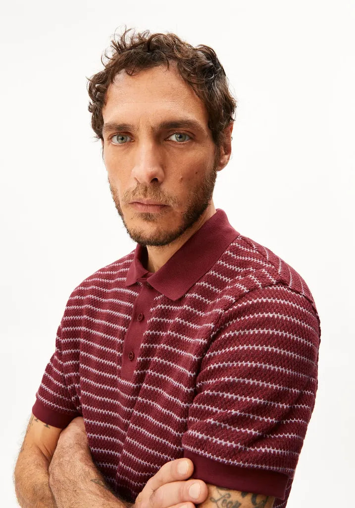 A man wearing a burgundy and white striped knit polo shirt, photographed against a clean white background.
