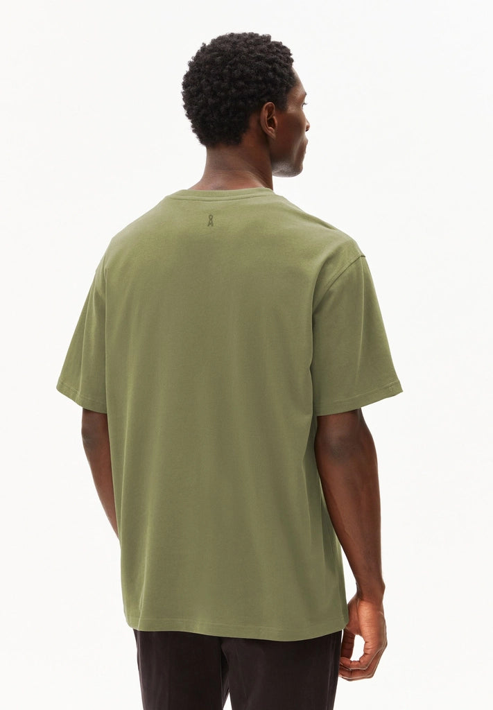 Back view of a man wearing the ARMEDANGELS Canada Maarkos Heavy Weight T-Shirt in fatigue green with black trousers on a white background.